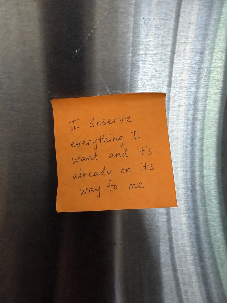 A handwritten sticky note on a fridge that reads I deserve everything I want and it's already on its way to me