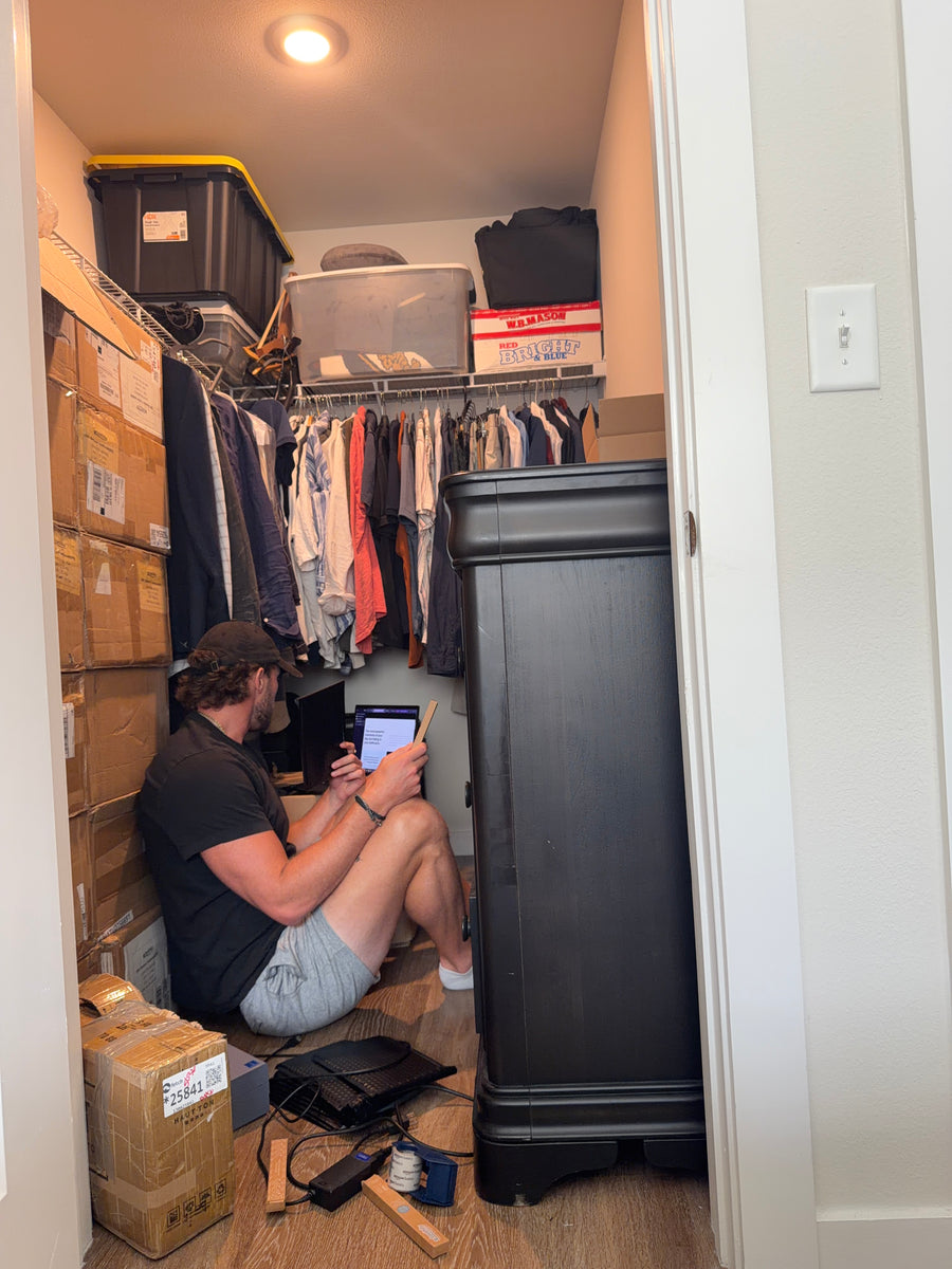 Anthony working on a laptop on the floor of a closet stacked with shipping boxes