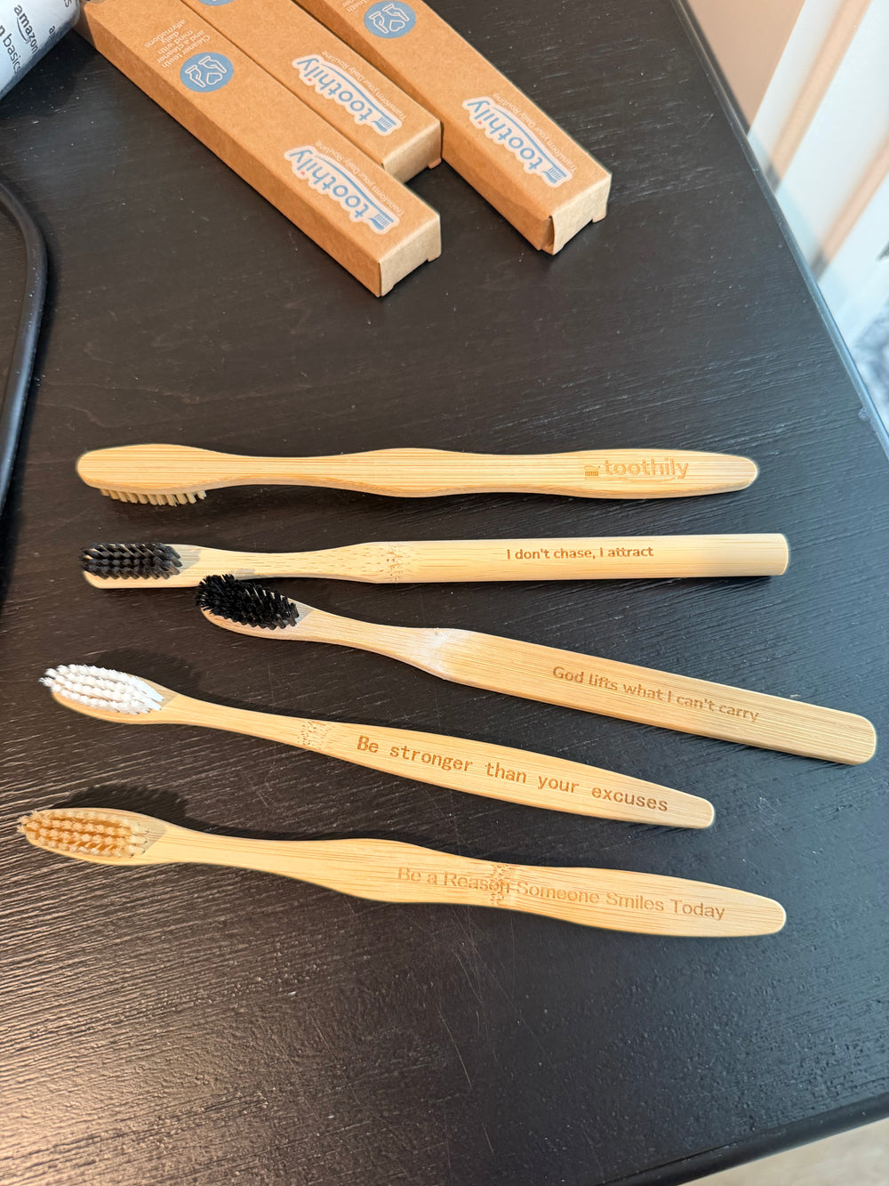 Five Toothily bamboo toothbrushes on a table, each engraved with a different message, beside their kraft boxes